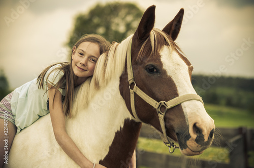 Young girl is sitting on a horse / Young girl is sitting on a horse, hugging it and smiling at the camera.