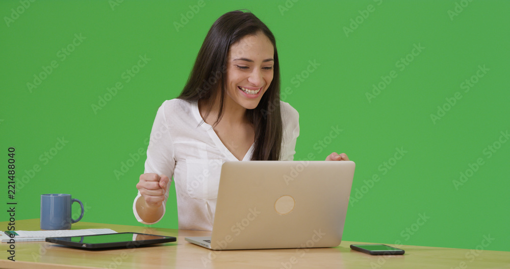 A Latina woman celebrates as she uses her laptop on green screen A Latina woman celebrates as she uses her laptop on green screen