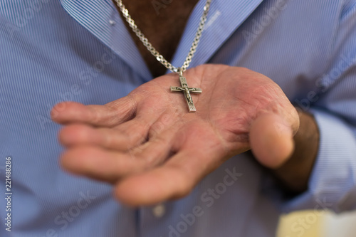 steel Catholic cross with a chain lies in the man's hand
