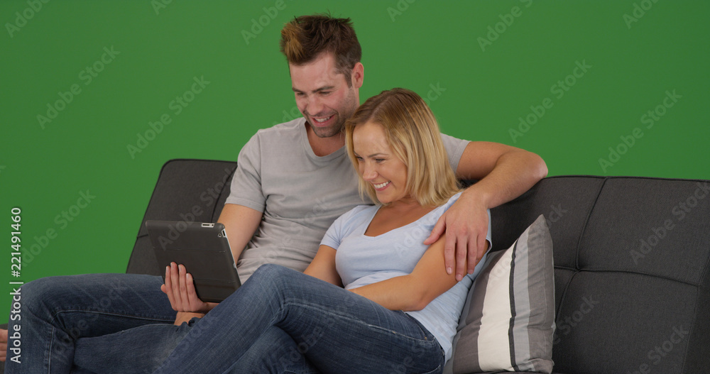 Loving young couple sitting on couch using tablet together on green screen