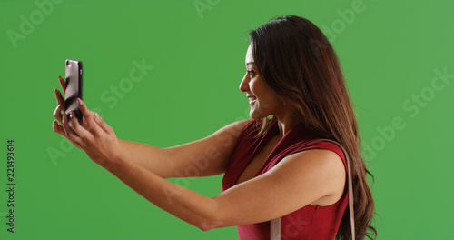 Attractive Latina woman using phone to take selfie on green screen