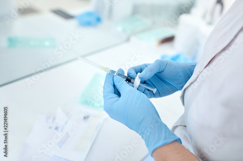 Hands of the beautician in blue gloves holding syringe. The cosmetologist prepares for a injection cosmetology procedure