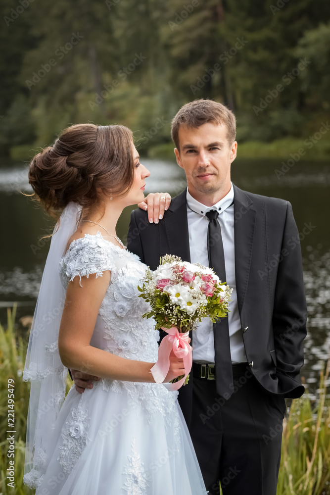 Happy wedding couple. Bride and groom are embracing in the park against the background of the pond. Sunny autumn day Happy wedding couple. Bride and groom are embracing in the park against the background of the pond. Sunny autumn day