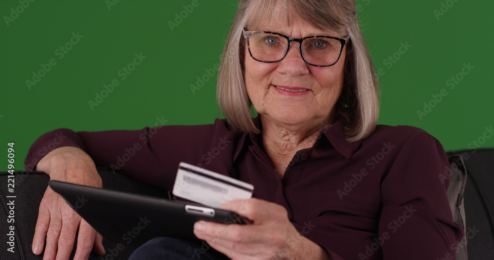 Charming old woman with tablet and credit card smiling at camera on green screen Charming old woman with tablet and credit card smiling at camera on green screen