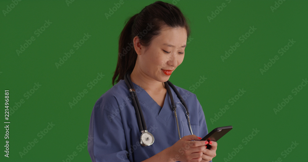 Asian female nurse with mobile device texting on green screen Asian female nurse with mobile device texting on green screen