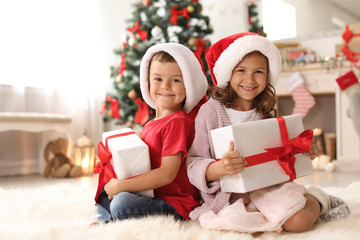 Cute little children in Santa hats with Christmas gift boxes at home