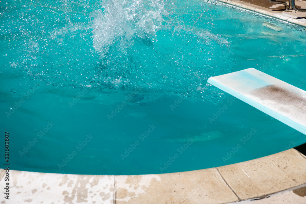 Woman under water after jumping off diving board in an outdoor swimming pool. Splash from water