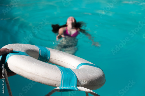 Man holding out life preserver to help young woman who is drowning in a swimming pool. Rescuing woman drowning in pool, focus on the lifesaver. Life guard reaching out holding white life saver.