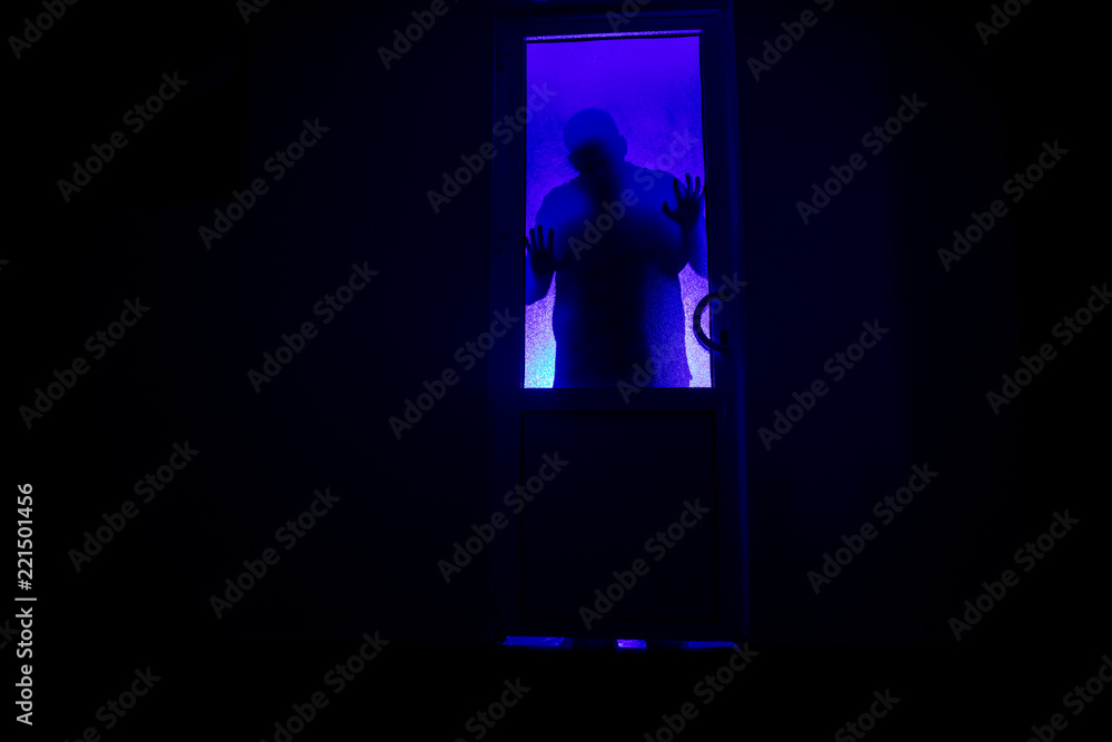 Silhouette of an unknown shadow figure on a door through a closed glass door. The silhouette of a human in front of a window at night. Scary scene halloween concept