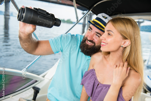 A young guy looks with a girl in binoculars on a yacht