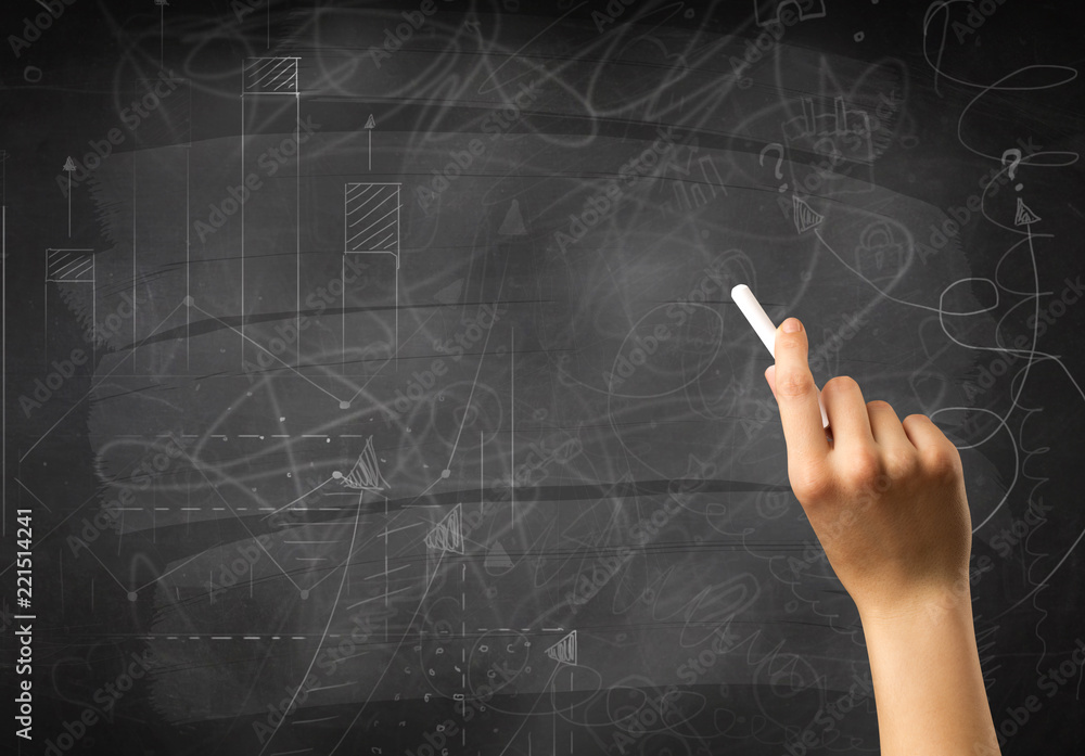 Fototapeta premium Female hand holding white chalk in front of a blackboard with scribbles and plans drawn on it 