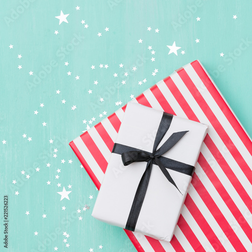 Closeup of beautiful Christmas gifts wrapped in white and striped gift paper decorated with ribbon and sparkling stars on turquoise wooden table. New Year, holidays and celebration concept