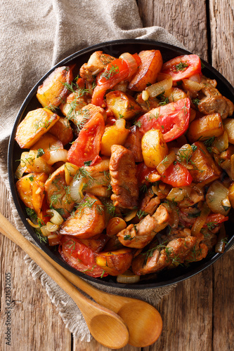 Ojahuri fried meat with potatoes, tomatoes, herbs and spices close-up on a frying pan. Vertical top view photo