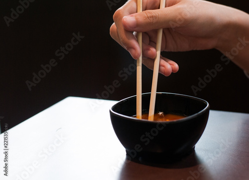 Chopsticks held by right hand is on the small bowl for shabu dipping with black background