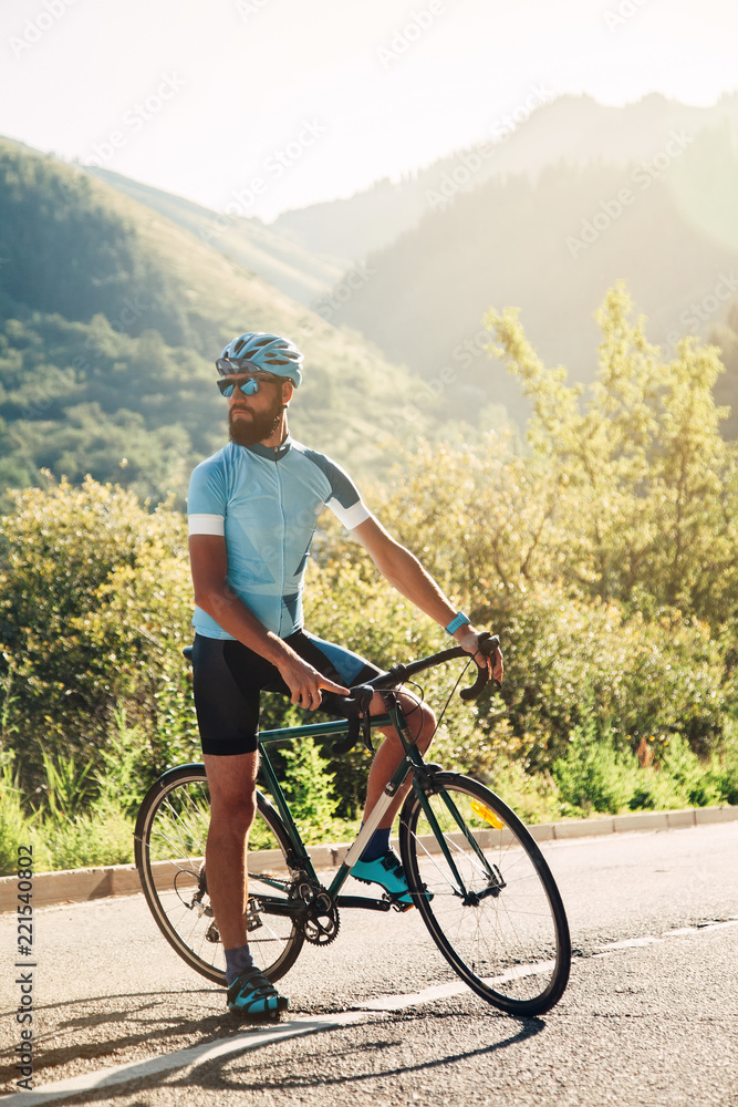 A man with a bicycle in the mountains. Road in the mountains covered with forest.