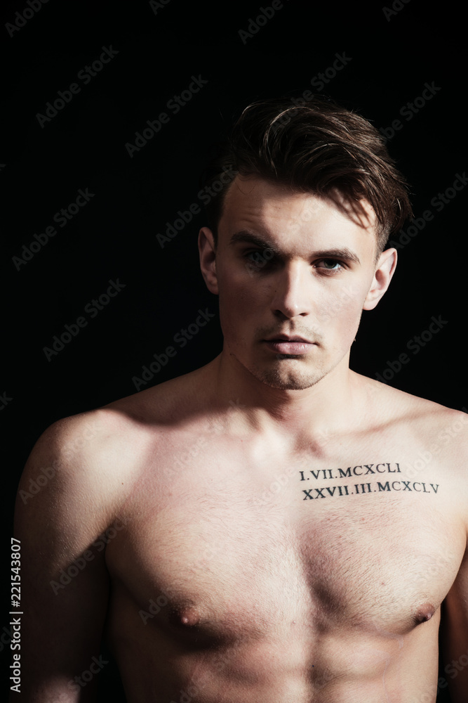 Macho on pensive face with muscular figure, sportsman, bodybuilder. Guy with tattoo looks confident and attractive. Sexy macho concept. Man with torso, muscular macho, shadow on body, dark background. Macho on pensive face with muscular figure, sportsman, bodybuilder. Guy with tattoo looks confident and attractive. Sexy macho concept. Man with torso, muscular macho, shadow on body, dark background.