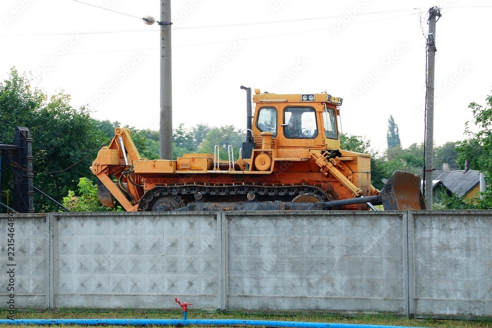 one large orange tractor stands at the concrete fence one large orange tractor stands at the concrete fence