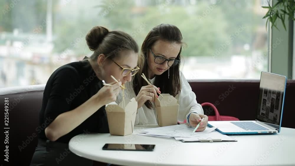 Two women spend brainstorming a business project in the office and eat noodles chopsticks Two women spend brainstorming a business project in the office and eat noodles chopsticks