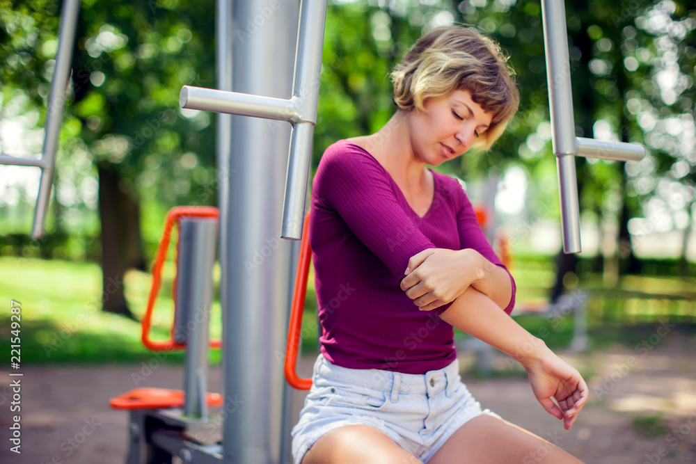 Fototapeta premium Young woman feeling pain in her elbow, hand during sport workout in the park. Sport, medicine and people concept