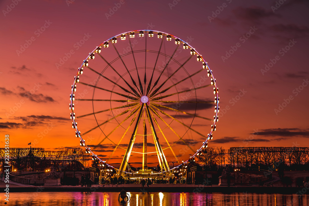 Illuminated ferris wheel with colorful sunset.