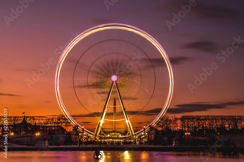 Illuminated ferris wheel with colorful sunset.