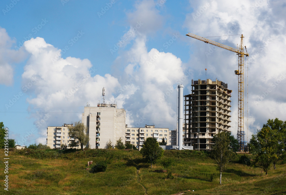 The basis of a house under construction, a working tower crane against the blue sky in summer weather.