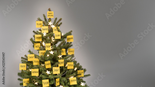 Christmas tree with decorations of 25 yellow post-it notes with business keywords and fairy lights in front of a light gray background, copy space, nobody 