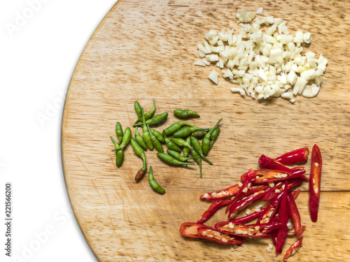 Chopped garlic, chopped red chili peppers and green tiny chilli peppers on the round wooden chopping board. White background, isolated.