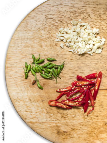 Chopped garlic, chopped red chili peppers and green tiny chilli peppers on the round wooden chopping board. White background, isolated.