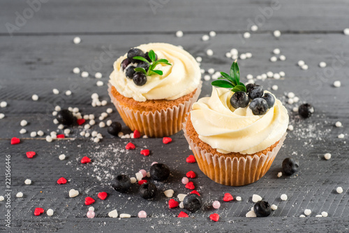 Creamy cupcakes with blueberries on the wooden background