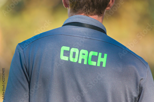 Back of sport coach wearing sport shirt with word Coach written on back