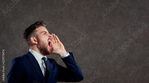 Young businessman with a beard screaming against a gray background.
