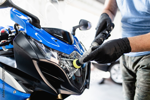 Motorcycle detailing - Man with orbital polisher in repair shop polishing motorcycle. Selective focus.