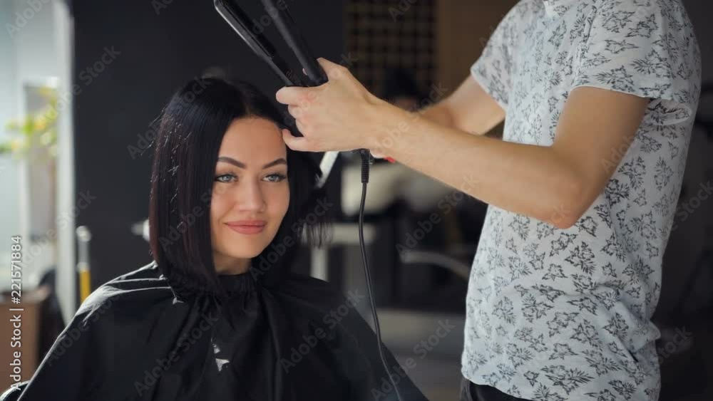 Beautiful woman happy while hairdresser is straightening her hair in salon. New haircut or hairstyle for young woman. Beautiful woman happy while hairdresser is straightening her hair in salon. New haircut or hairstyle for young woman.