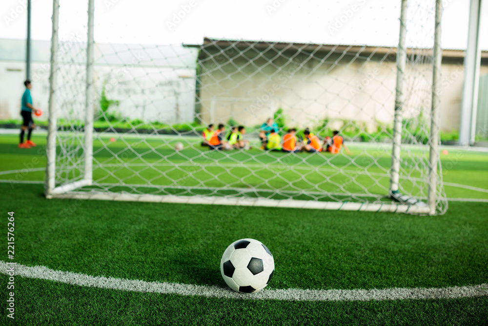 Fototapeta premium Football on green artificial turf with blurry soccer players background.