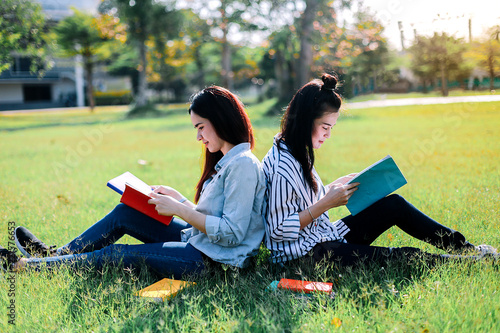 Asian women are happy and relaxed by reading book on green grass before attending class in the morning.