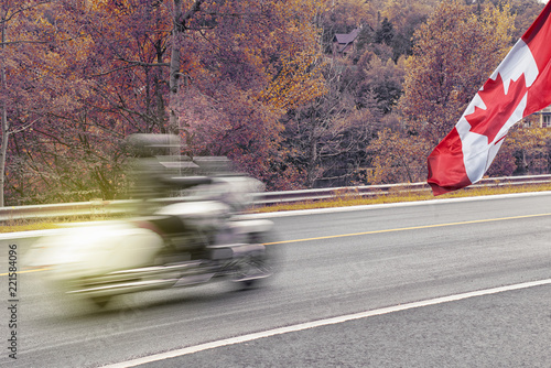 Closeup shot of a motorcycle in motion during fall season with Canadian flag waving