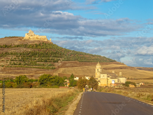 A prominent castle in ruins up on the hill and the Church of Santa María del Manzano along the road - Castrojeriz, Castile and Leon, Spain photo