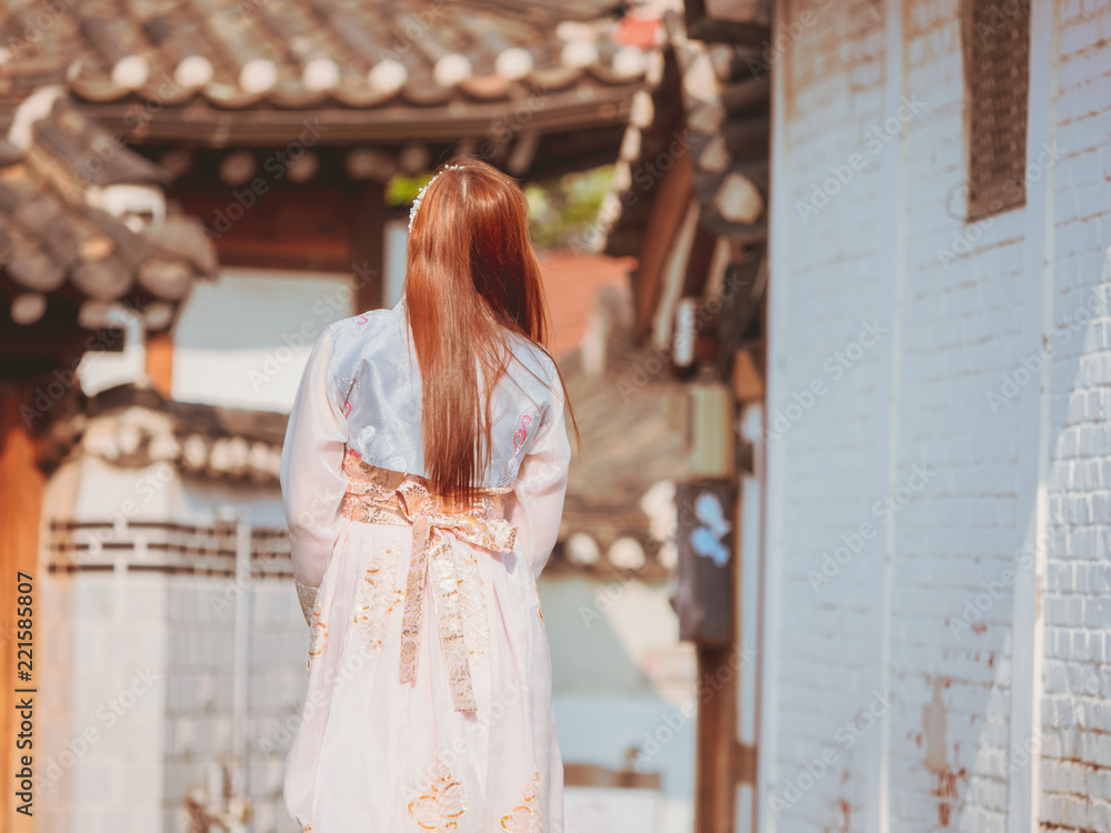 Naklejka premium travel and tourist asia concept from backside long hair woman in korea traditional cloth (hanbok) relax, take picture in vintage town with rim light and soft focus background