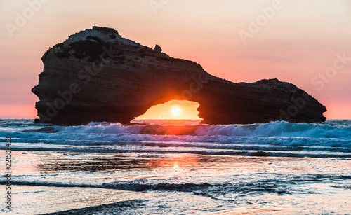 Sunset on a beach in Biarritz with the sun in the center of a rock's hole. Basque country of France.