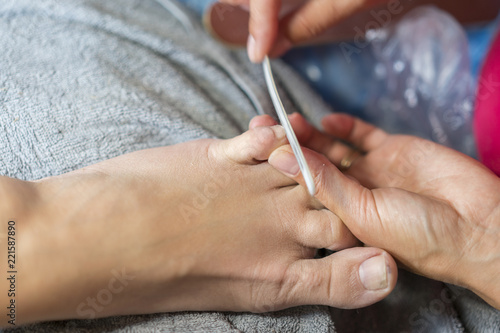 Hands in gloves cares foot nails. Pedicure beauty salon. Fingernails filing with file. close up