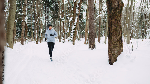 Young man exercising at winter, running through the forest