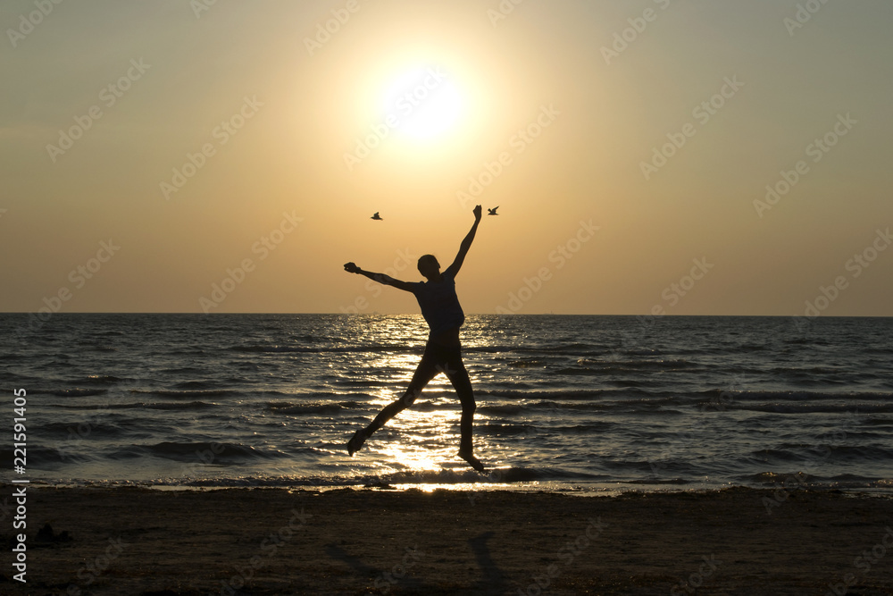 silhouette of a girl who jumps against the background of the sea and sunrise