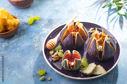 baked figs with goat cheese,walnuts and honey on ceramic plate and blue concrete background, selective focus