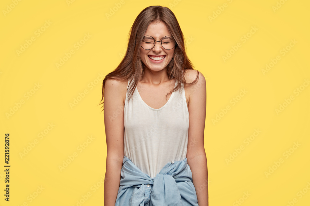Funny emotive teenager with overjoyed expression, closes eyes from pleasure, laughs at good joke, dressed in casual outfit, isolated over yellow background. People and positive emotions concept Funny emotive teenager with overjoyed expression, closes eyes from pleasure, laughs at good joke, dressed in casual outfit, isolated over yellow background. People and positive emotions concept