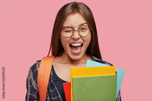 Fotografi Isolated shot of optimistic Caucasain girl blinks eyes, opens mouth widely, has