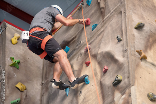 Young man practicing rock climbing on artificial wall indoors.