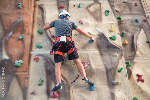 Young man practicing rock climbing on artificial wall indoors.