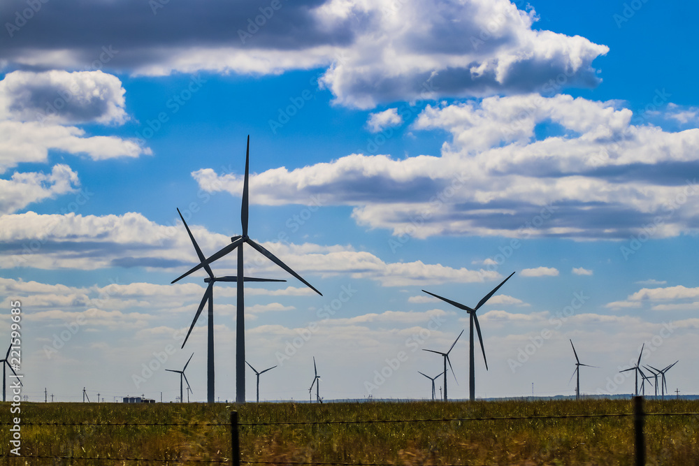 Wind turbine on Oklahoma prarie behind barbed wire fence - selective focus - under blue cloudy sky Wind turbine on Oklahoma prarie behind barbed wire fence - selective focus - under blue cloudy sky