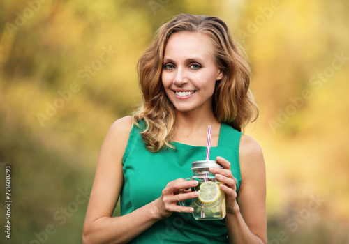 Kobieta w zielonej sukience trzymająca kubek z woda cytryną i mięta